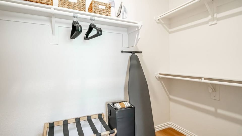 Walk-in closet includes an iron, ironing board, Pack 'n Play, storage baskets, and luggage rack, offering plenty of space for your clothes and essentials.