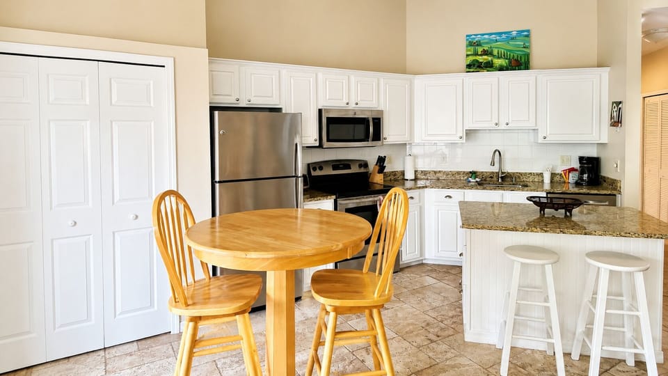 Open kitchen and dining area featuring white cabinetry, granite countertops, stainless steel appliances, and breakfast bar seating.