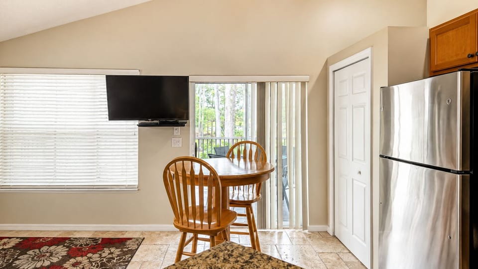 Dining area with a round table, wall-mounted TV, balcony access, and easy flow into the kitchen.