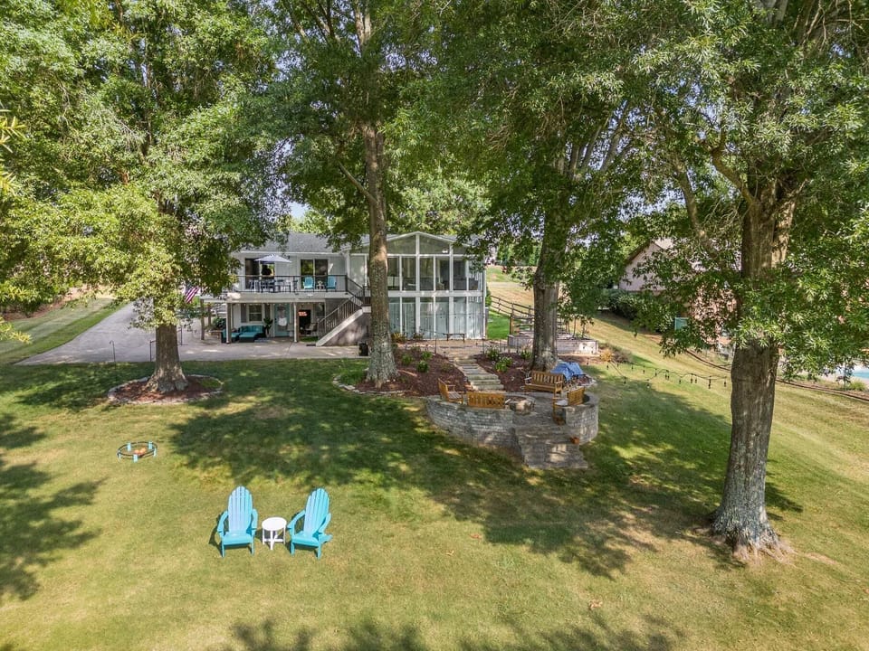Bird's-eye view of our lakeside haven: an open backyard with lush grass, cozy fire pit area, benches, and shady trees.