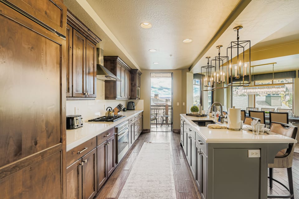 This chef-inspired kitchen boasts warm wood cabinetry, a large marble island with seating for four, and elegant lantern pendant lights. Perfect for hosting, the open layout is both stylish and functional.