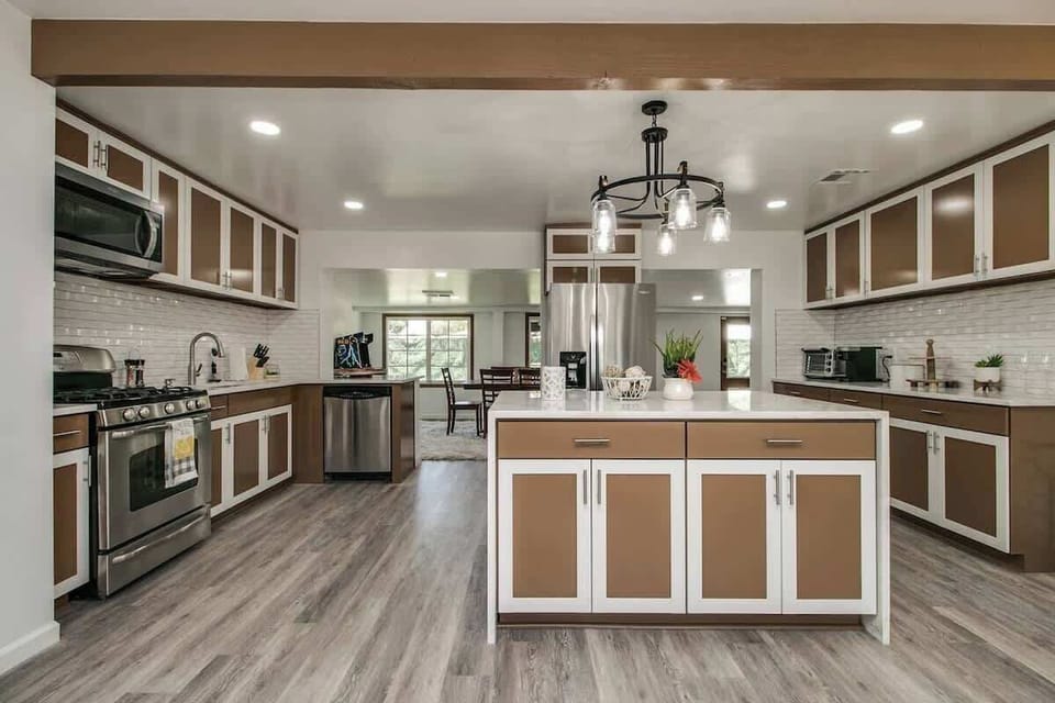 Cook together around the central island, surrounded by wood-tone cabinets, bright recessed lights, and stainless appliances—plenty of counter space for chopping and plating.