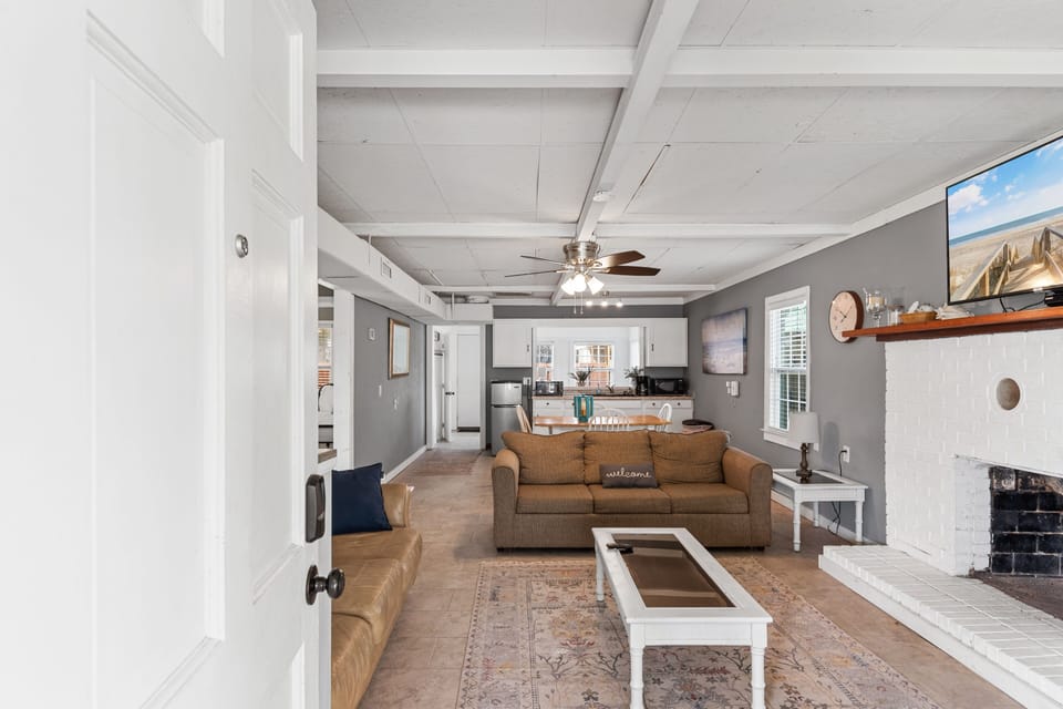Relax in your open-plan living space featuring cozy seating, exposed beam ceilings, and a welcoming fireplace for perfect evening gatherings.