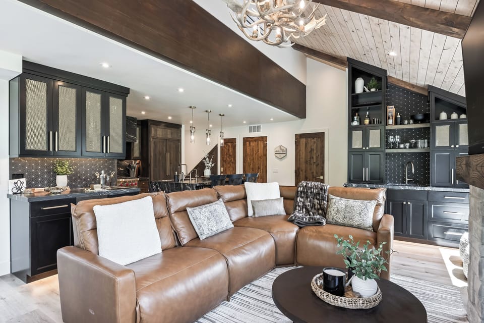- Relax in the living room with plush leather sectional and soft throws  
- Vaulted wood ceilings and antler chandelier add rustic charm  
- Sip drinks at the wet bar with black cabinetry and glass display