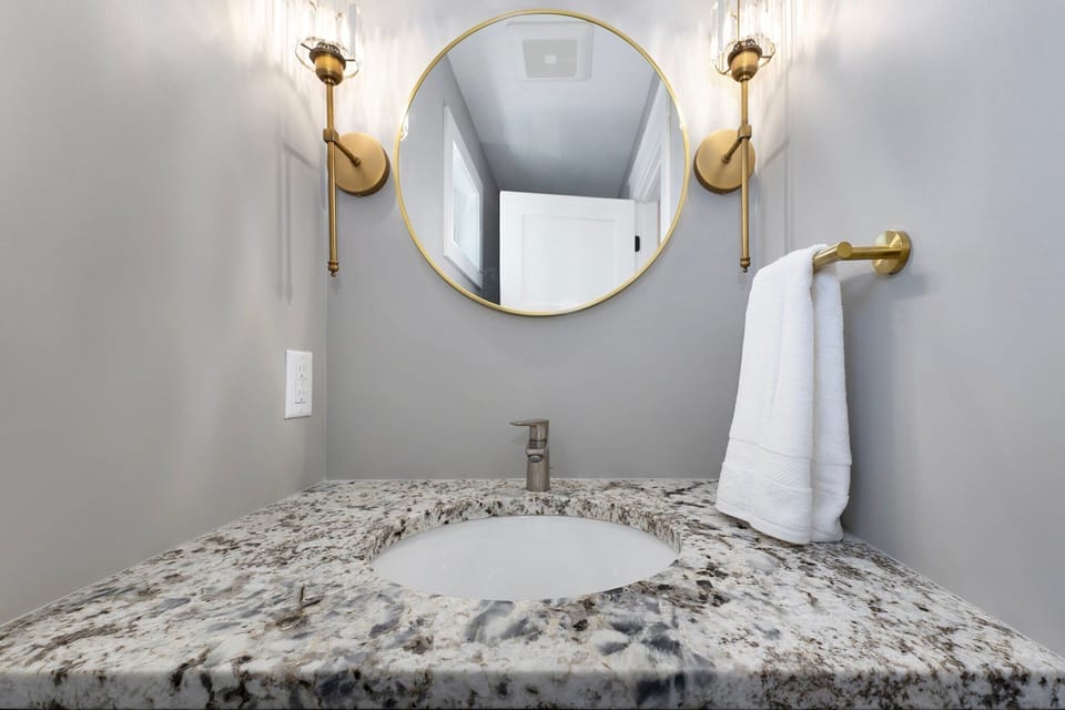 Patterned stone vanity with an inset sink below a round mirror and brass wall lights.