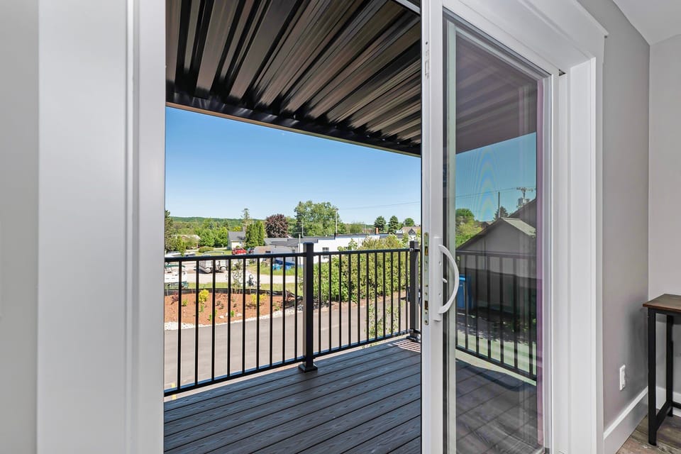 Sliding glass door opening to a covered balcony with black railings and neighborhood views.