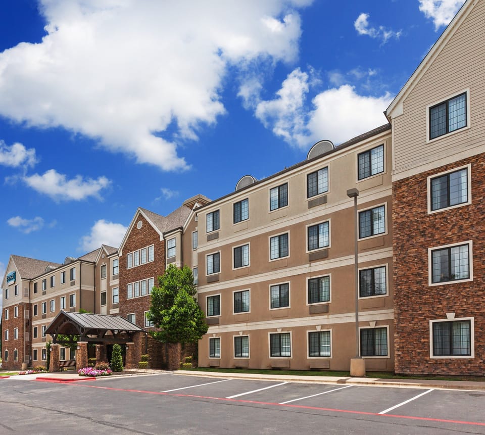 The exterior of the hotel showcases its charming architecture and well-maintained landscaping against a bright blue sky.