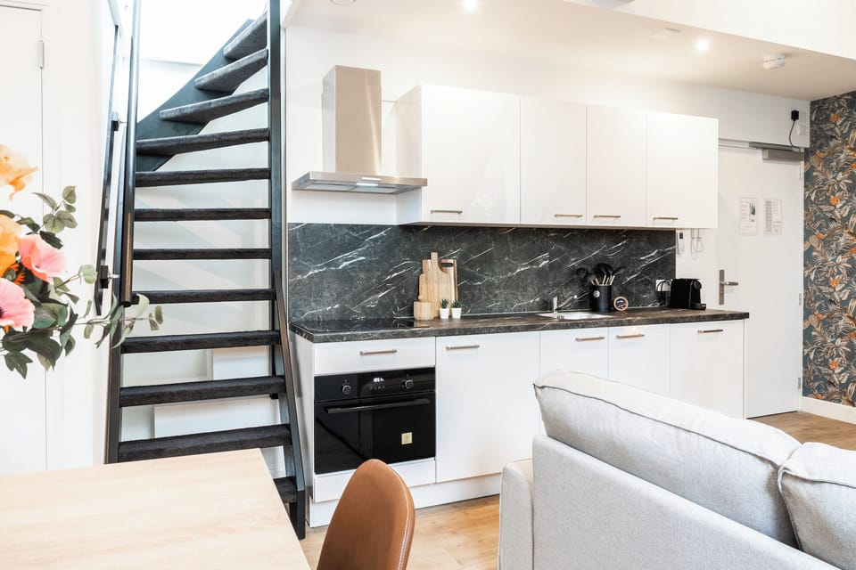 The kitchen is ideally situated next to the living area, complete with a sofa and a staircase, creating a seamless flow between cooking, lounging, and upper-level access.