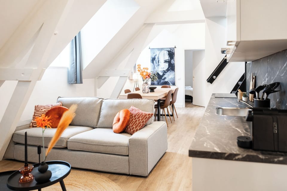 A bright and modern living space with a comfortable sofa, stylish décor, and a sleek kitchen corner, creating a functional and cozy environment.