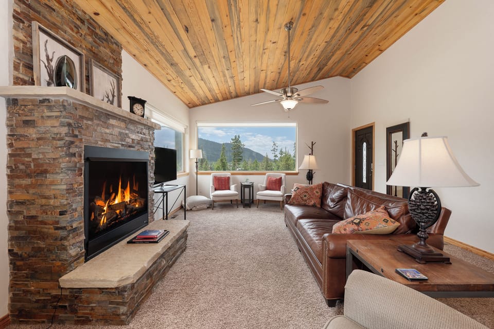 - Living room with stone fireplace and leather sofa   - Large windows frame scenic Rocky Mountain views   - Cozy cabin space for relaxing after outdoor fun