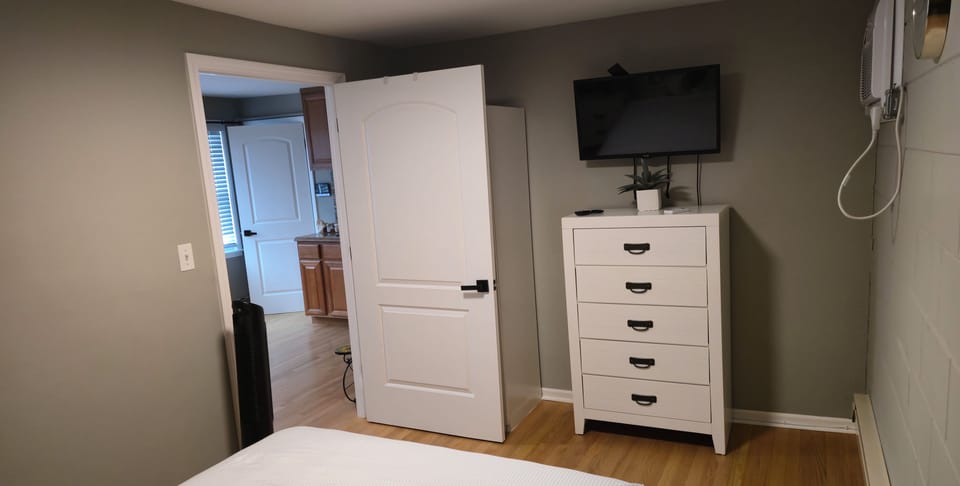 Bedroom with full-size bed with rose and white accents. Climate control heat and wall air conditioner with smart television. wardrobe closet with extra blanket and sheets for twin beds. There is also hanging ironing board and iron.