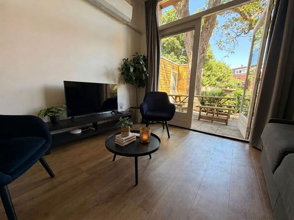 Modern living area with smart TV, comfortable seating, and direct access to a private terrace surrounded by greenery.