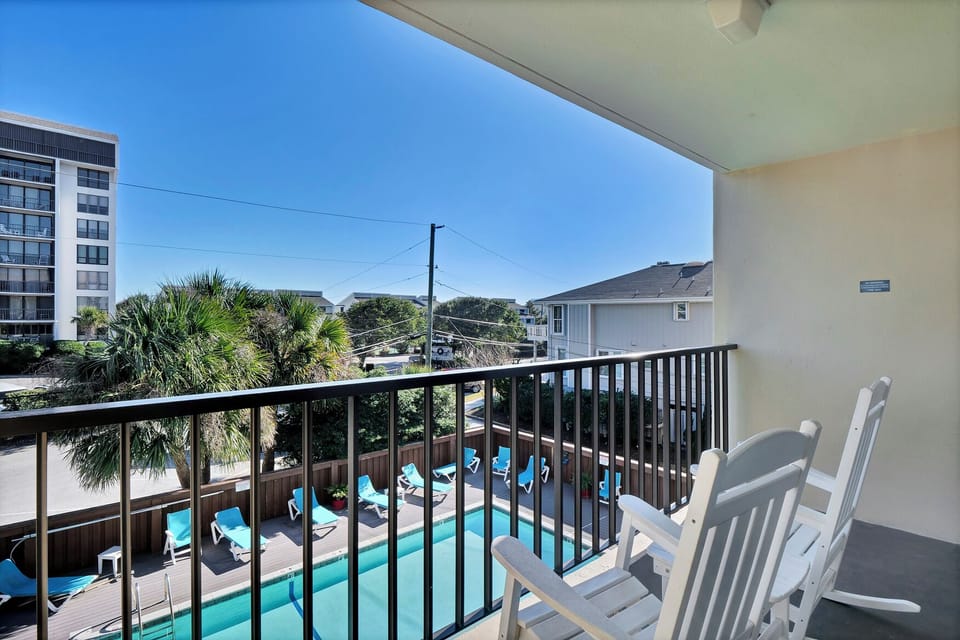 Relax on your private balcony with comfortable seating while enjoying views of the pool area below and tropical palms beyond.