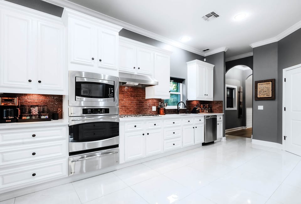 Bright white kitchen with double oven, gas stove, and dishwasher, accented by warm copper backsplash