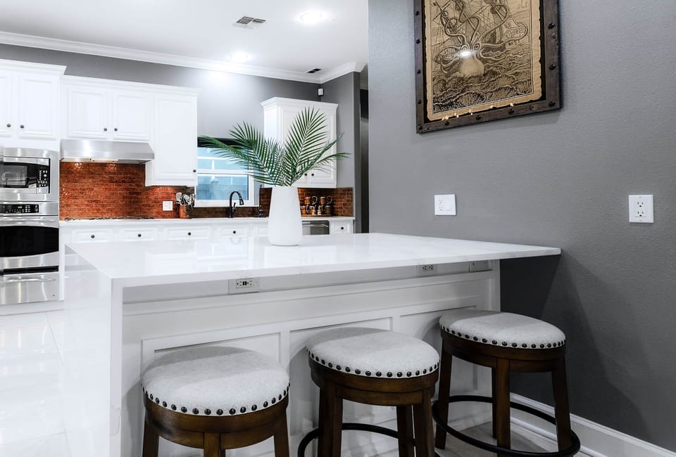 Bright white island with marble-style countertop, tropical greenery, and nautical art on display.