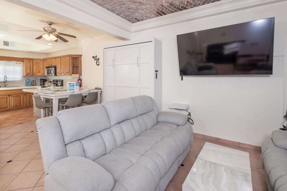 Spacious living room featuring plush reclining sofas, a large TV, and vaulted brick ceiling with ceiling fan perfect for relaxing after a day at the beach.