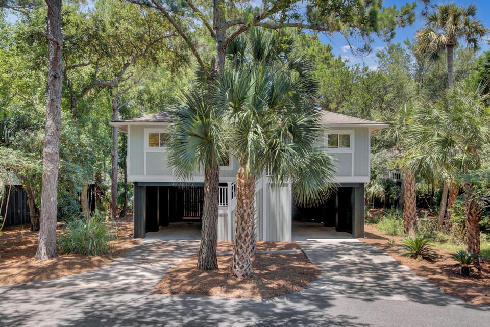 Cozy elevated duplex nestled under tall pines and palms, with shaded carports and a peaceful wooded setting.