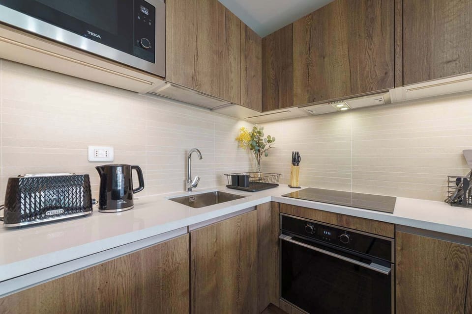 Sleek, modern kitchen with all essentials for a comfortable stay, including a stovetop, microwave, and stylish wooden cabinetry.