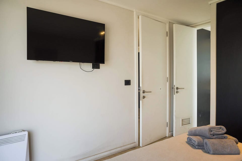 Relax in a cozy bedroom with a wall-mounted TV and fresh towels for your comfort.