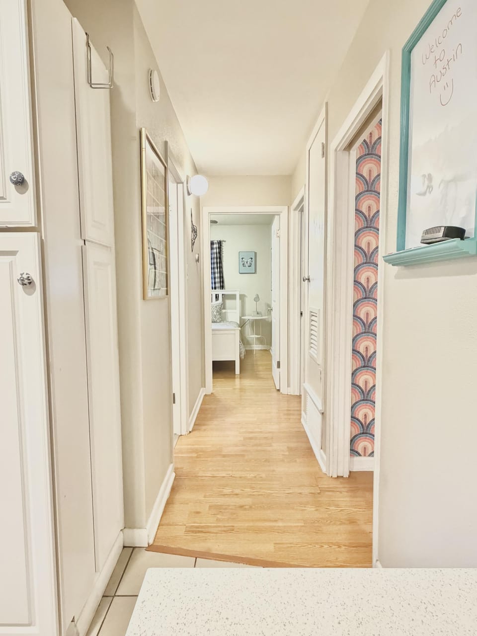 Hallway with light wood flooring and soft beige walls leading to a bedroom with patterned curtains.