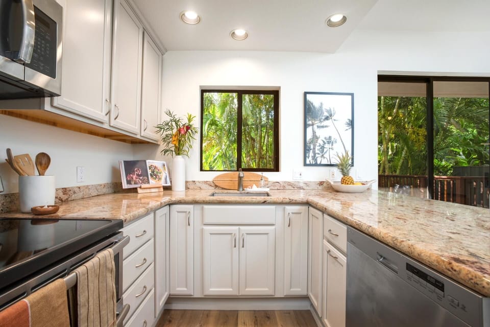This airy, modern kitchen features granite counters, sleek appliances, and views of lush tropical greenery outside   