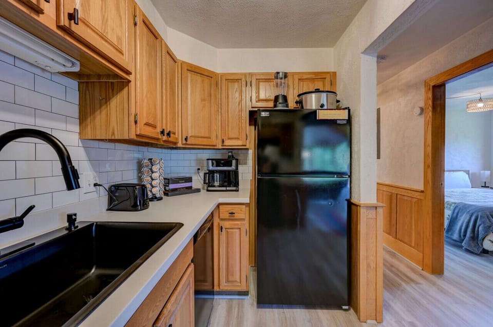 Fully equipped kitchen with warm wood cabinetry, modern black appliances, and all essentials for cooking a delicious family meal. Enjoy ample counter space, a coffee maker, and stylish subway tile.