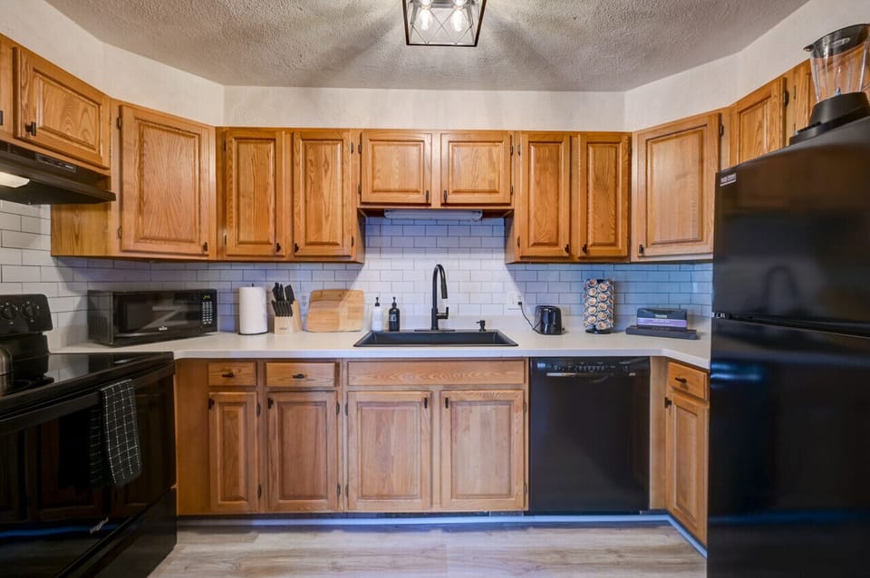 Fully equipped kitchen with warm wood cabinetry, modern black appliances, and all essentials for cooking a delicious family meal. Enjoy ample counter space, a coffee maker, and stylish subway tile.
