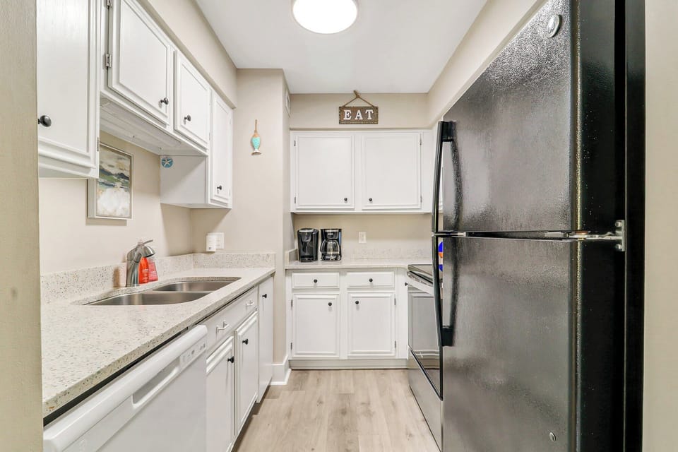 Speckled stone countertops and crisp white cabinetry create a bright, efficient space for morning coffee. Smooth black appliances anchor this tidy kitchen, offering a clean and modern spot to prep your favorite vacation meals.