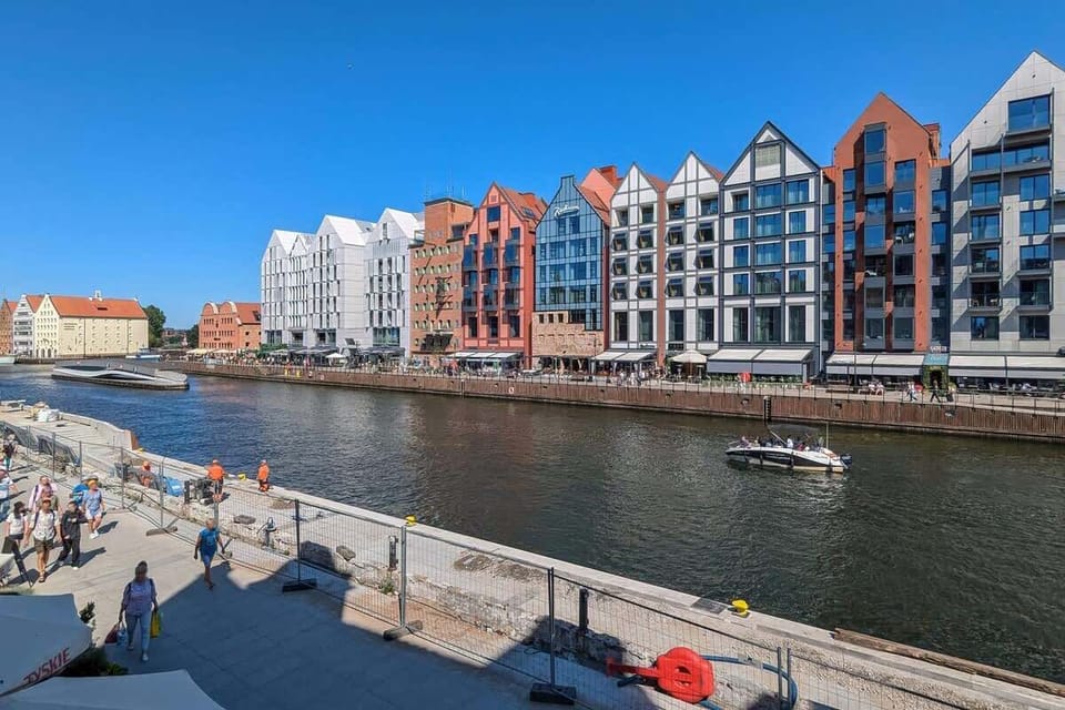 A different perspective of the colorful canal-side buildings, with cafe umbrellas lining the street below. The cobblestone walkway suggests a lively, walkable area.