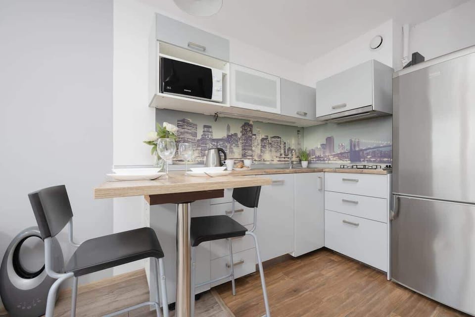 A compact kitchen with white cabinets, tiled backsplash, and a dining area with two chairs.