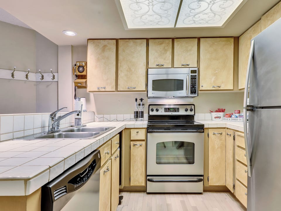 Fully equipped kitchen with stainless steel sink, microwave, electric stove and oven, refrigerator, coffee maker, cooking utensils, and ample cabinetry—everything you need to prepare meals and feel at home.