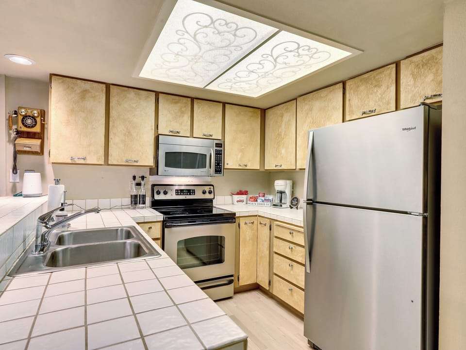 Fully equipped kitchen with stainless steel sink, microwave, electric stove and oven, refrigerator, coffee maker, cooking utensils, and ample cabinetry—everything you need to prepare meals and feel at home.