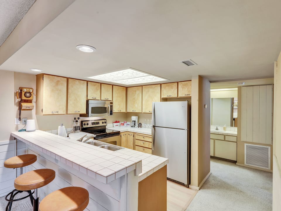 Fully equipped kitchen with stainless steel sink, microwave, electric stove and oven, refrigerator, coffee maker, cooking utensils, and ample cabinetry—everything you need to prepare meals and feel at home.
