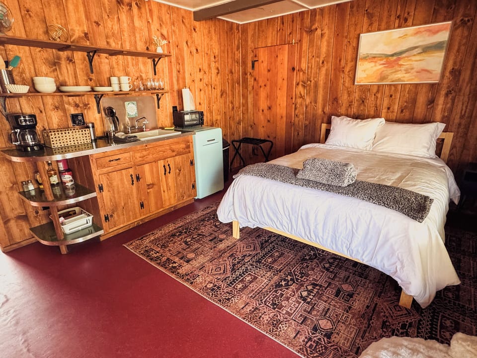 Rustic wood-paneled room with queen bed, kitchenette, and vintage mini fridge