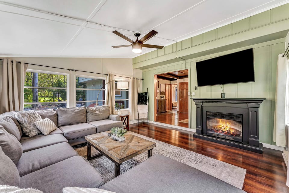 Step into the sunroom, where a second inviting living area features plush sectional sofas, a 60" TV, and a cozy wood-burning fireplace, perfect for relaxation and entertainment.