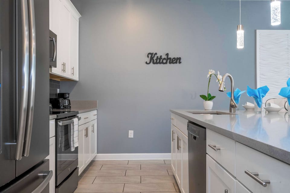 Channel your inner chef in this contemporary kitchen with a polished quartz island sink, ample cabinetry, and a stylish grey‐blue accent wall labeled “Kitchen.”