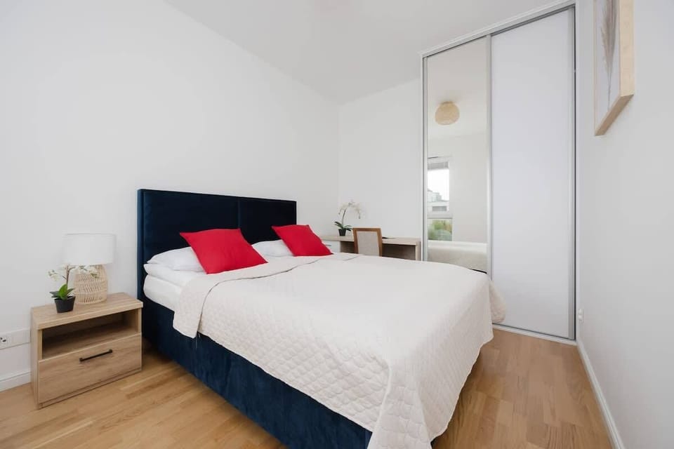 A minimalistic bedroom with a comfortable double bed, navy blue headboard, and red accent pillows, offering a peaceful sleeping area.