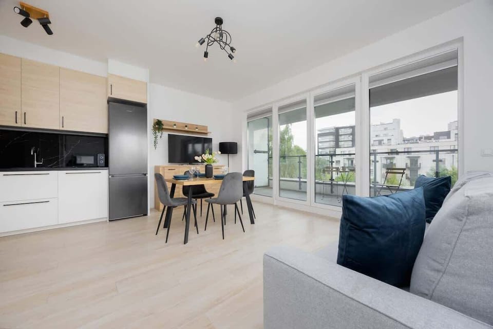 A bright and modern open-plan lounge with a round dining table and large windows that flood the space with natural light.