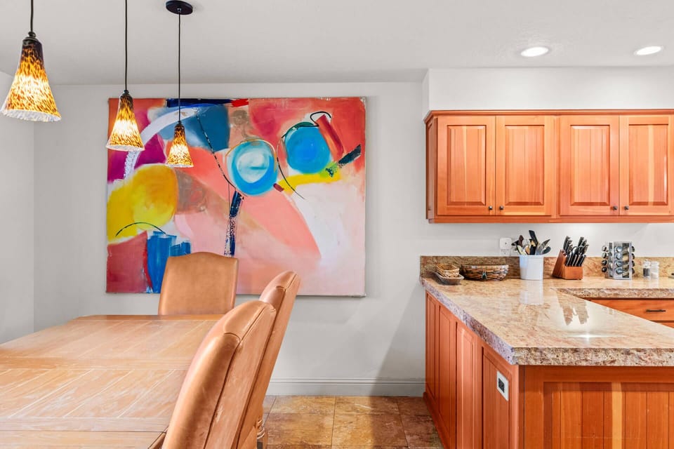 Your open kitchen and dining area blends warm wood cabinetry with vibrant art, creating an inviting space where you can cook and gather under charming pendant lighting.