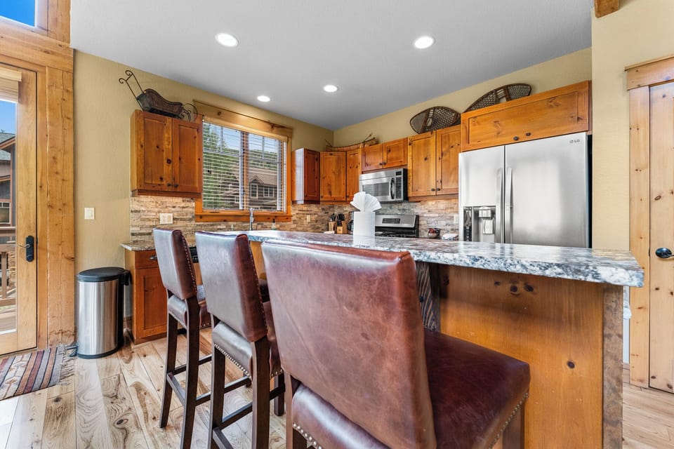 Breakfast bar with seating for three and full-size kitchen with granite countertops and stainless steel appliances.