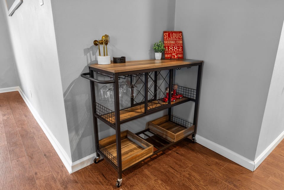 Rolling wood-and-metal serving cart with glassware, trays, bottle storage, and St. Louis decor.