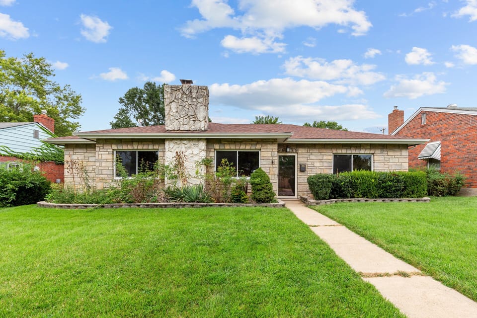 Front view of the single-story stone-faced home, lawn, walkway, and central entrance.