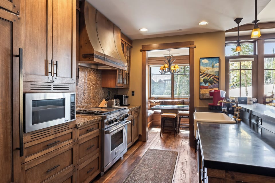 - Fully equipped kitchen with granite countertops and chef grade appliances
- Custom wood cabinetry, coffee station, and open layout for easy meal prep
- Dine under antler lighting in a sunlit breakfast nook with forest views