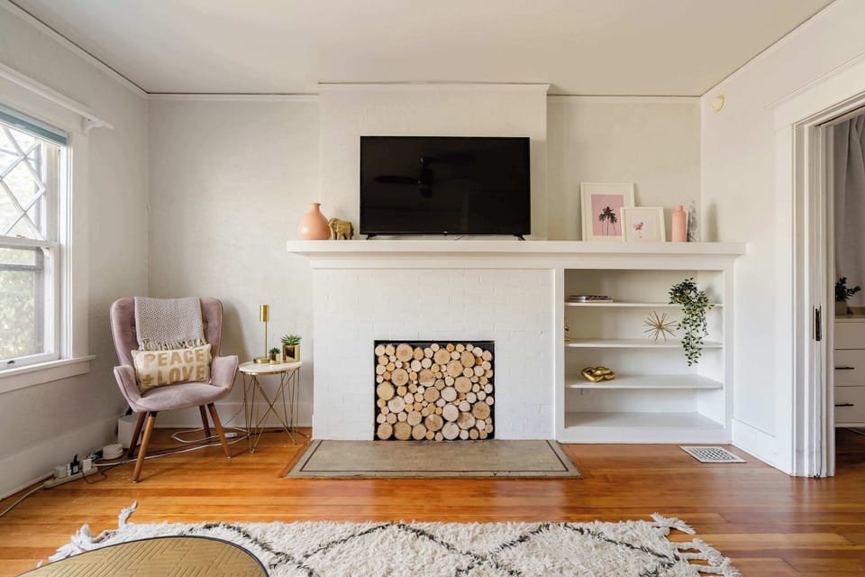 Television above a fireplace surround filled with decorative logs.