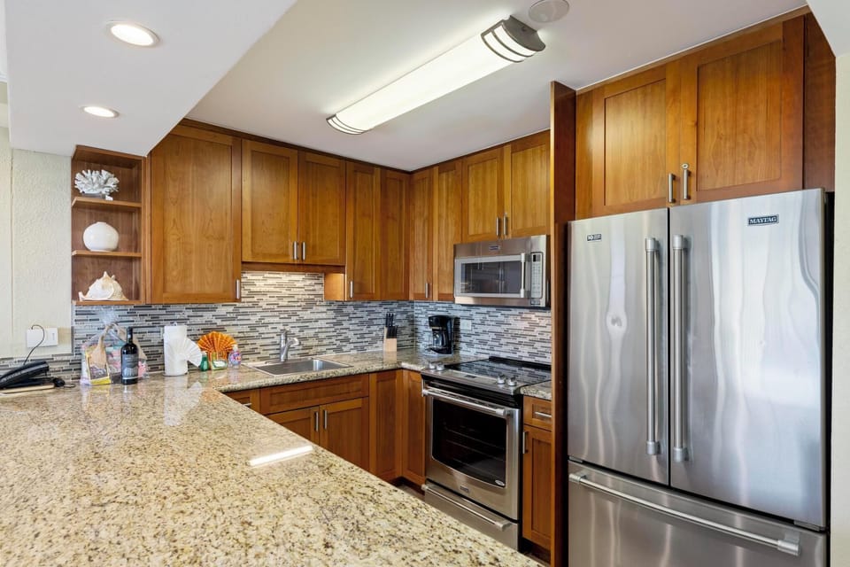 This fully equipped kitchen features stainless steel appliances, granite countertops, and a stylish tile backsplash—perfect for preparing meals during your Maui getaway.