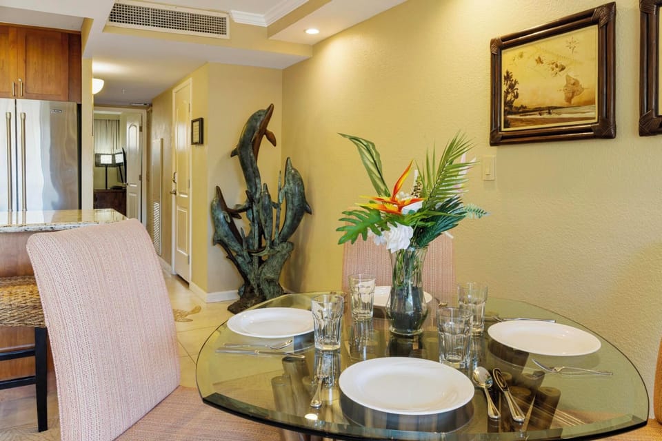 Gather around the glass-top dining table with plush seating and a vibrant floral centerpiece. The open layout offers easy access to the kitchen and resort-style ambiance.