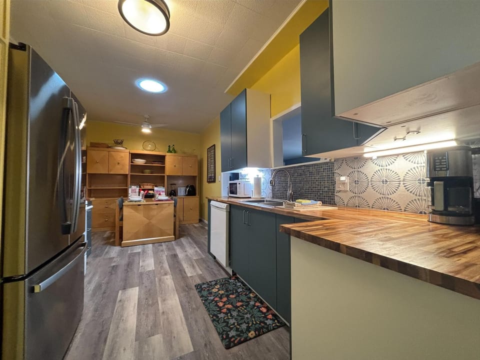 Wood countertops stretch along blue lower cabinets with a patterned tile backsplash in the kitchen.