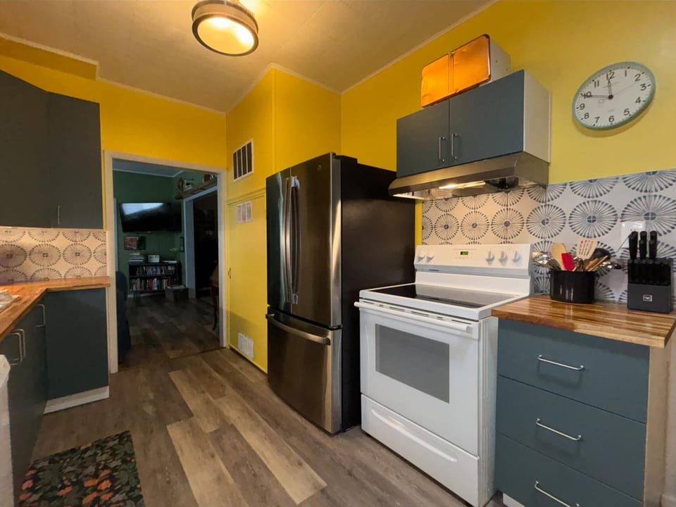 Yellow walls and patterned tile backsplash brighten the kitchen with stainless fridge and white electric stove.