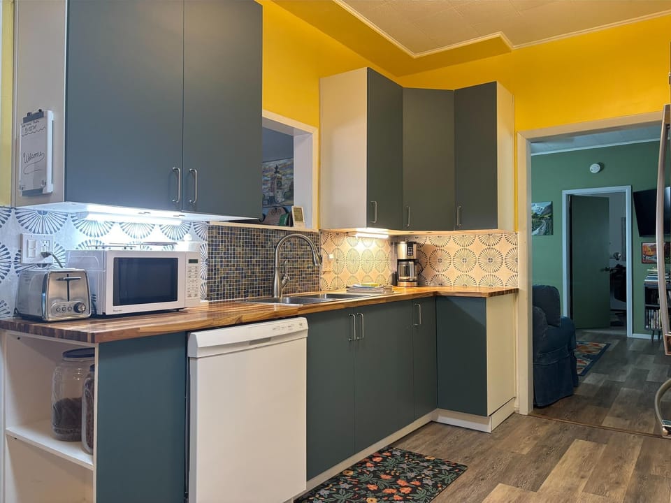 Green cabinets and butcher block counters contrast with yellow walls and patterned tile backsplash in the kitchen.