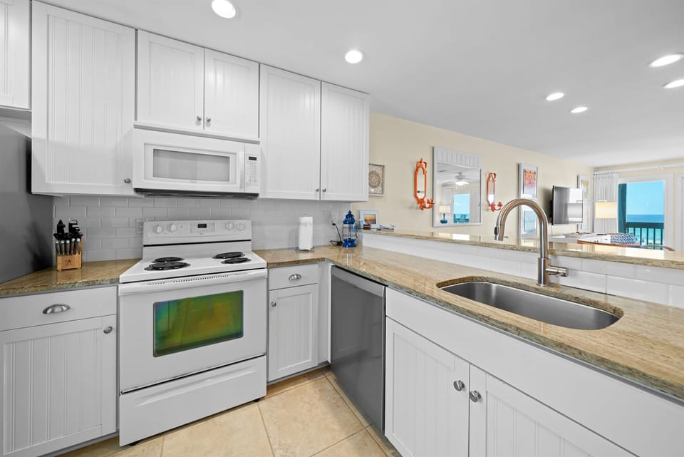 Your fully equipped kitchen features granite counters, modern appliances, and ocean views through the open living area.